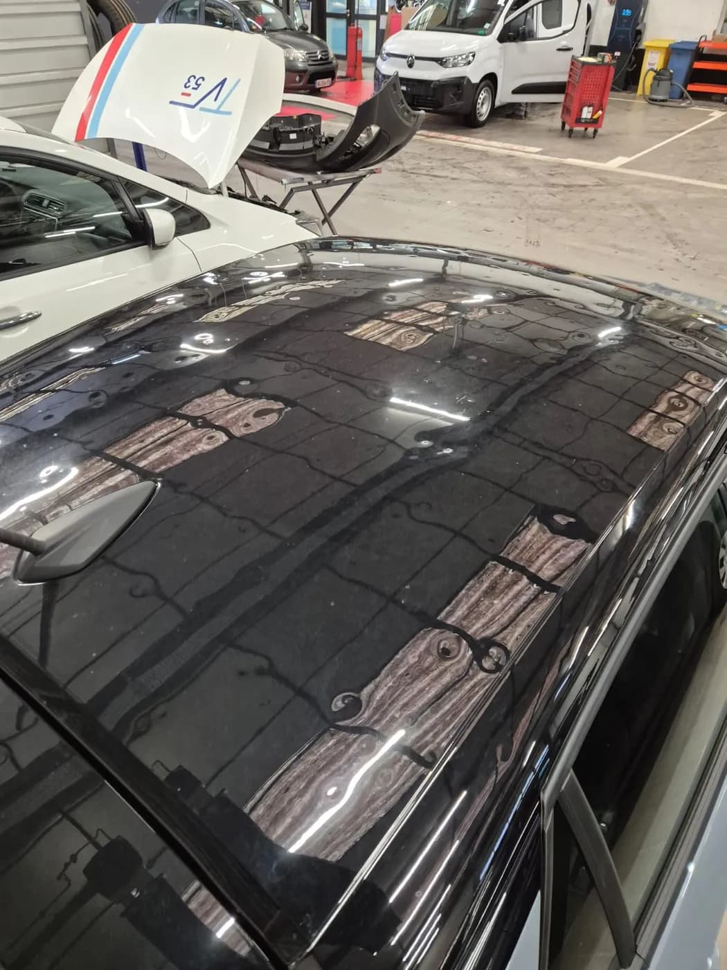 Avant — toit d'une voiture noire couvert d'impacts de grêle puis remis à neuf