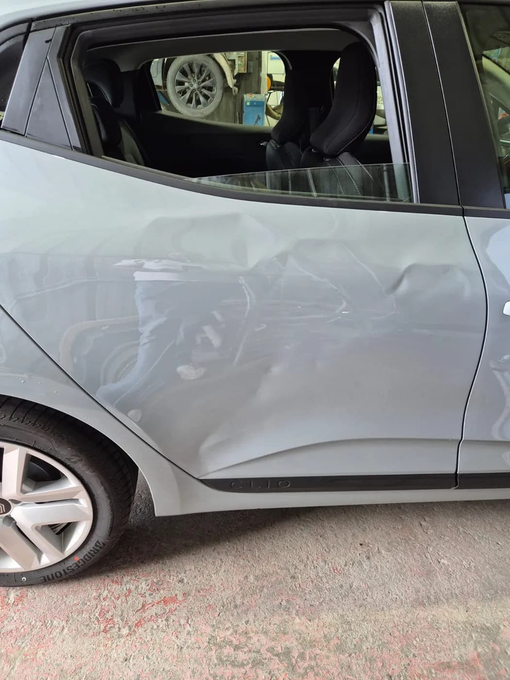 Avant — portière arrière fortement enfoncée d'une Renault Clio grise, redressée sans peinture